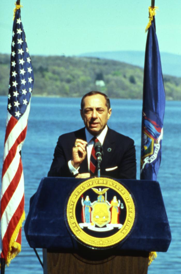 Governor Mario Cuomo giving a speech in front of a body of water