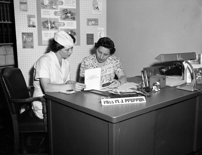 Two Health Department employees reading a book about meal planning, 1959