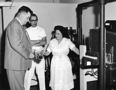 Two men and a woman inspecting scientific equipment, 1961