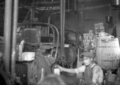 Men working at machinery:  narrow aisles, piles of boxes