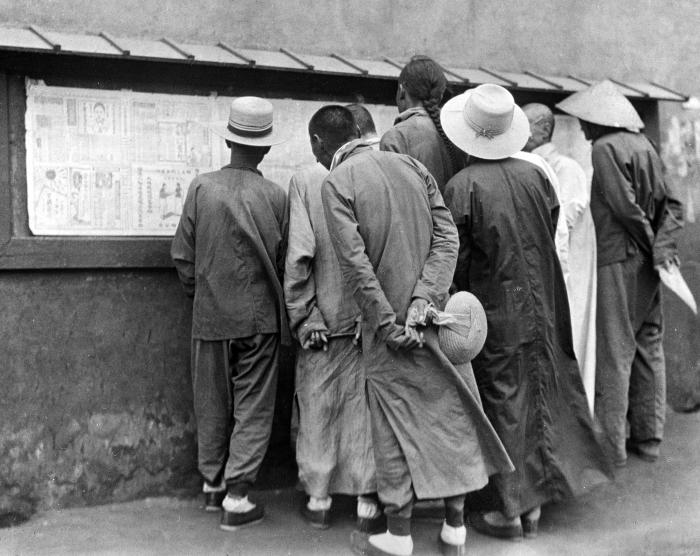 Men reading newspapers on bulletin board, China