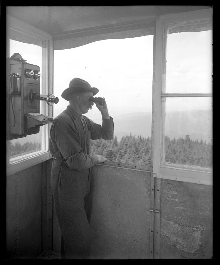 An observer with field glasses in the CC's forest fire observation station on the lookout for smoke